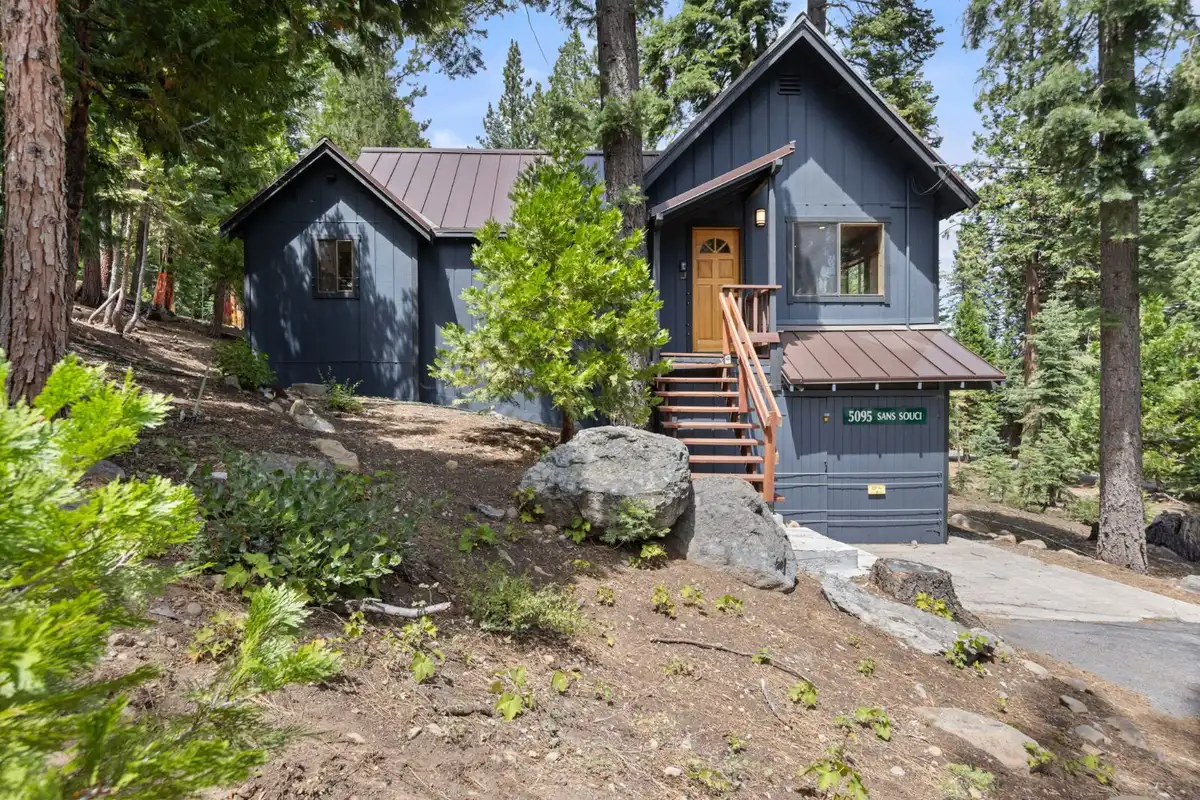 Dark blue cabin with a metal roof and front stairs among pines, Homewood Cabin in the Pines