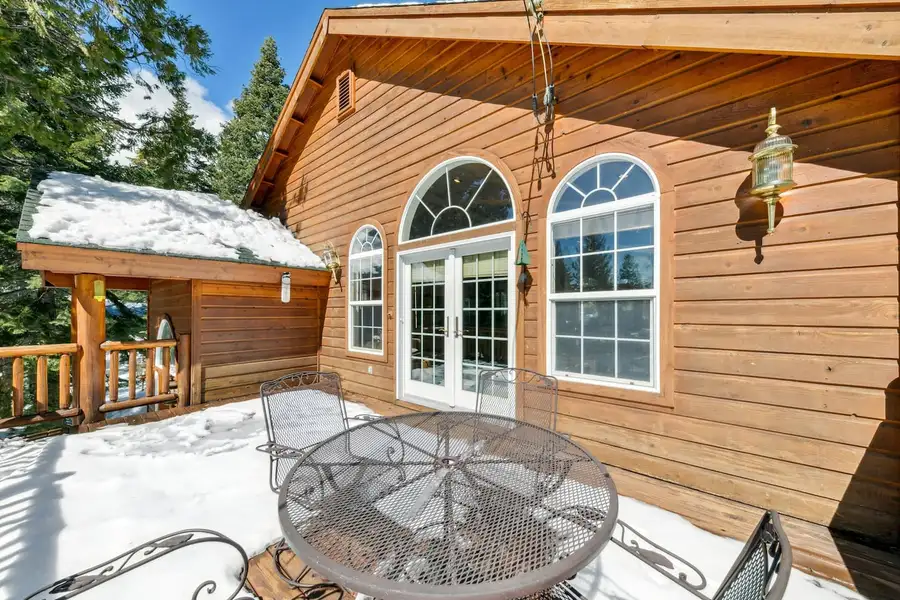 Snowy deck with a metal table beside arched windows, Hastings Hideaway Cabin