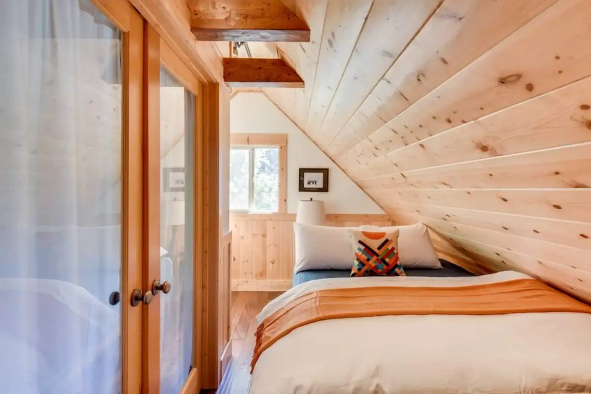 Bedroom with a sloped pine ceiling seen through glass doors, Tranquil Trails Cabin
